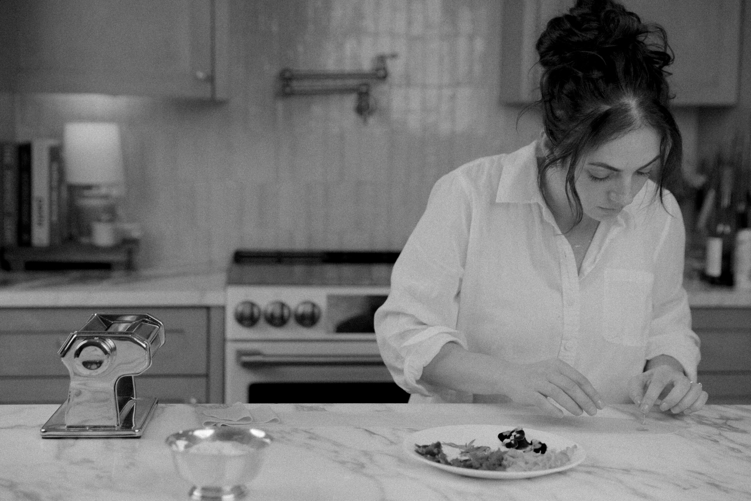 Private Chef Sherry Brubaker located in Pensacola, FL near Pensacola Beach that is in the Gulf Coast is preparing homemade pasta at a kitchen counter. There is a pasta maker and the image is in black and white with light film grain. 