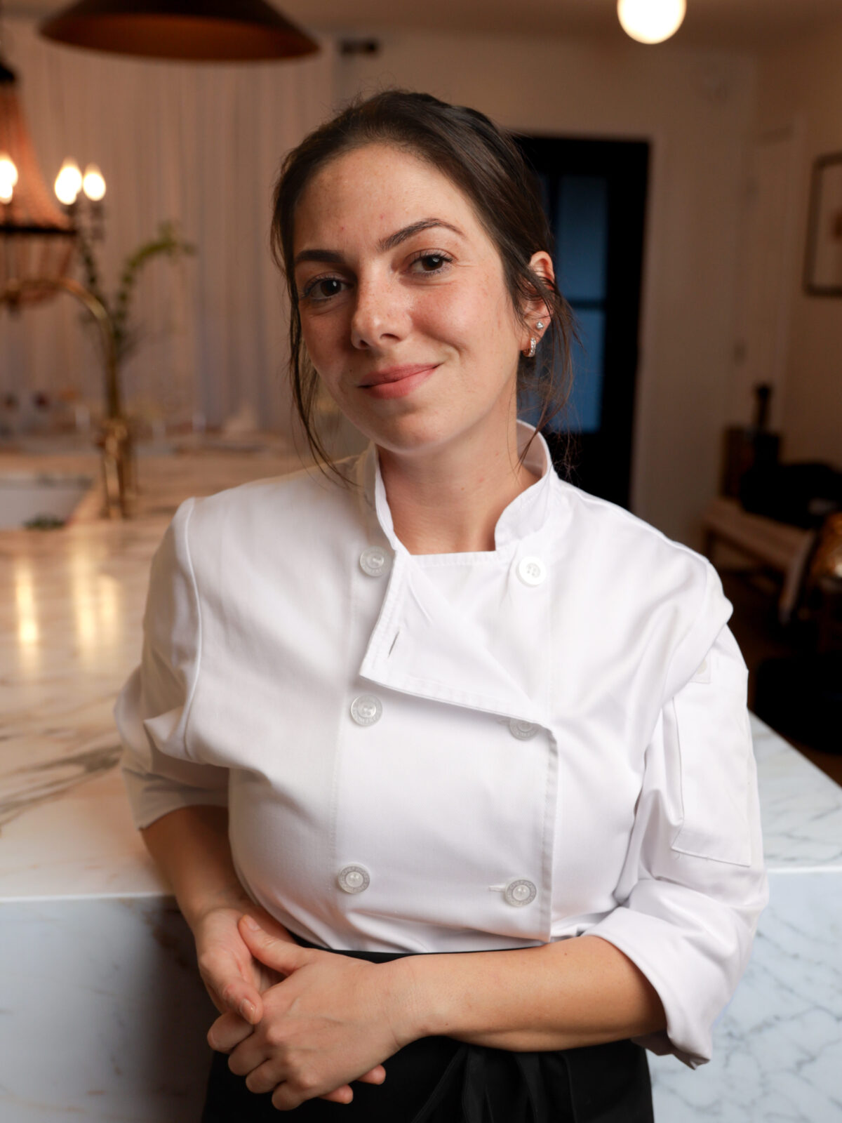 A photo of Chef Sherry Brubaker in her uniform posing in front of a chef's kitchen. 